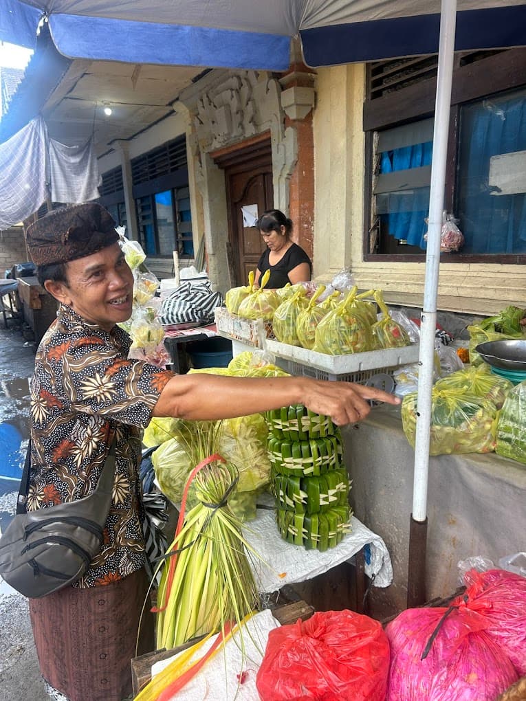 A morning market stall piled with chilies, shallots, and garlic, with a guide in a blue apron